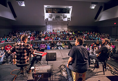 three musicians from behind with crowd of students in auditorium